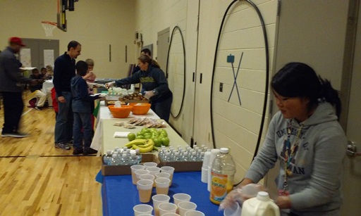 Kids are handed some drinks with a teacher prepares cups of juice.